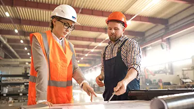 Beratungssituation in einer Werkhalle, TÜV Beraterin mit Produktionsmitarbeiter in einer Werkhalle