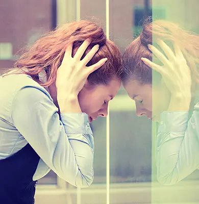 gestresste Frau hält sich den Kopf und lehnt gegen eine Glasscheibe